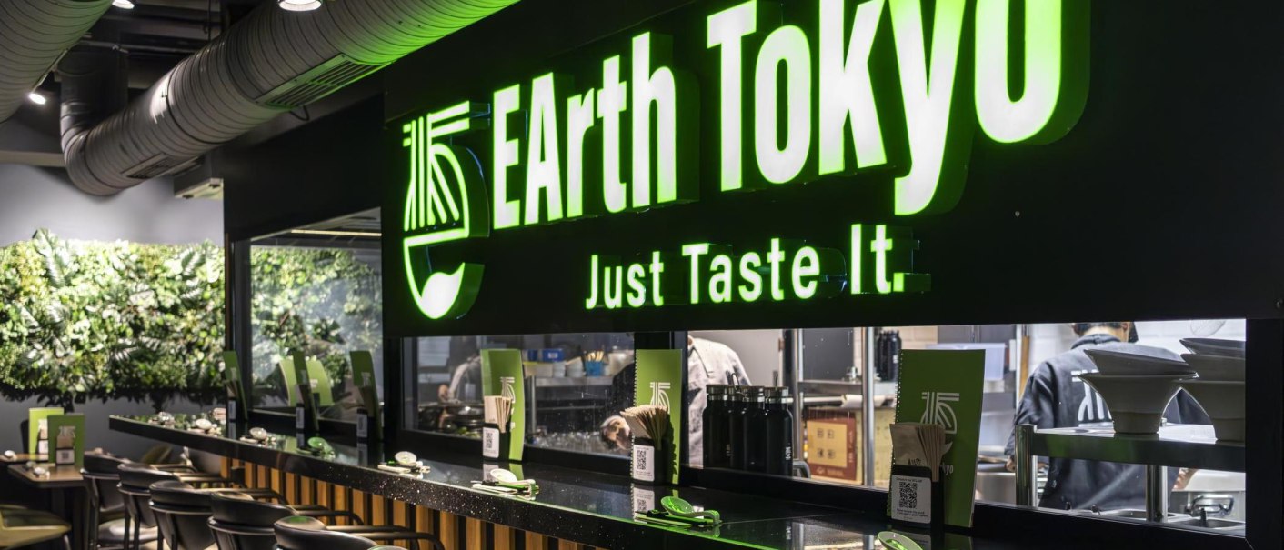 Restaurant with green illuminated sign 'EArth Tokyo' and the slogan 'Just Taste It'. Modern interior with plant wall., © SMG, Sarah Schmid
