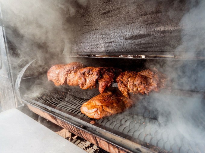 Mehrere Fleischstücke werden in einem Smoker gegrillt, umgeben von dichtem Rauch. Perfekt für ein Winter-BBQ., © Cool-Tours StattReisen Mehrere Fleischstücke werden in einem Smoker gegrillt, umgeben von dichtem Rauch. Perfekt für ein Winter-BBQ., © Cool-Tours StattReisen