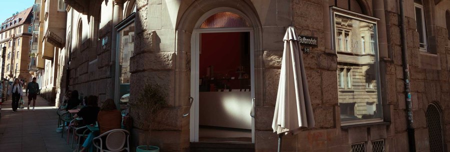 A caf&eacute; on Gutbrodstra&szlig;e with outdoor seating. People sit at tables while others walk along the street., &copy; SMG