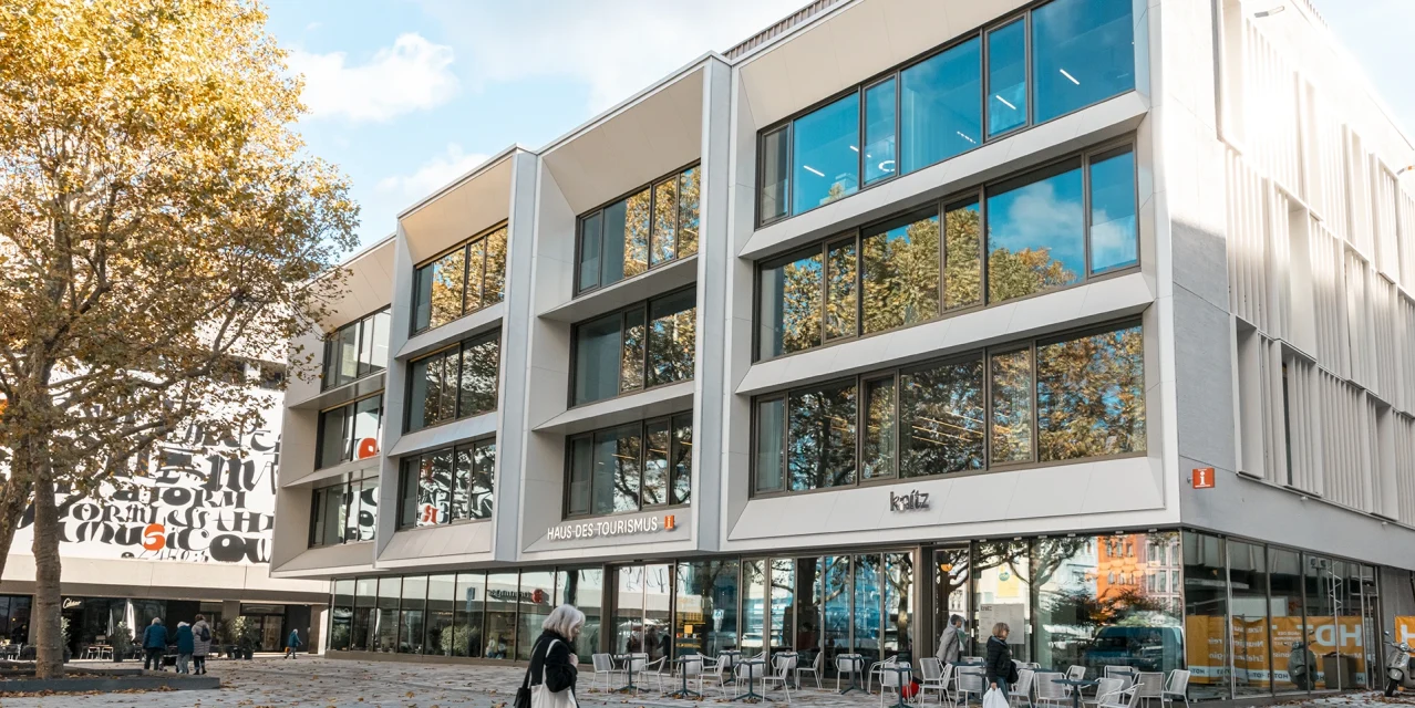 Außenfassade des Hauses des Tourismus mit moderner Glasfront, Platz und Passanten vor dem Gebäude., © SMG, Sarah Schmid Außenfassade des Hauses des Tourismus mit moderner Glasfront, Platz und Passanten vor dem Gebäude., © SMG, Sarah Schmid