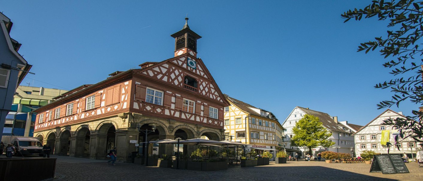 Half-timbered houses on Waiblingen's market square in sunny weather. People are strolling, a café with parasols can be seen. The sky is clear and blue., © SMG Stuttgart Marketing GmbH - Sarah Schmid