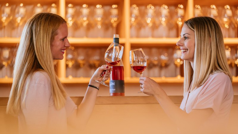 Two women clink glasses of wine in a wine shop. Wine bottles and glasses can be seen in the background., © Stuttgart-Marketing GmbH, Thomas Niedermüller