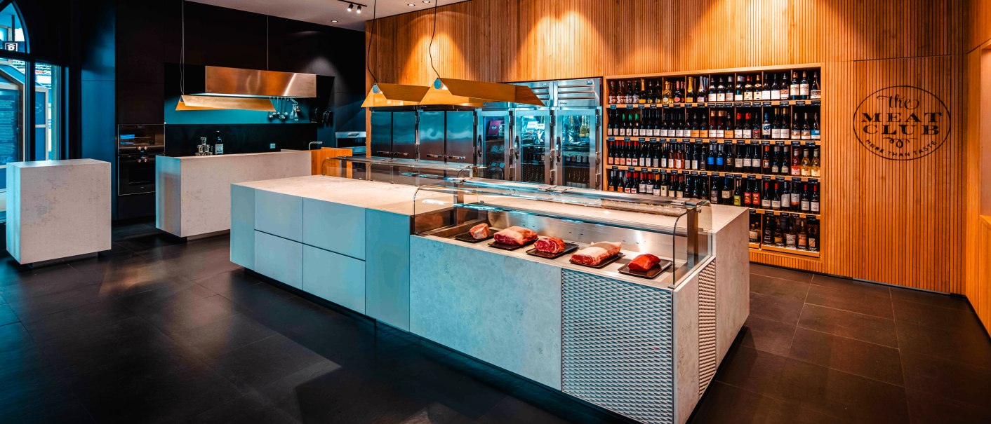 Modernes Fleischgeschäft mit eleganter Theke, Fleischpräsentation und großem Weinregal an der Wand. Stilvolle Beleuchtung und Holzverkleidung., © The Meat Club, Stuttgart