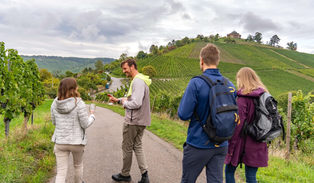 People walking along a wine trail, holding wine glasses. Vineyards and the burial chapel on a hill in the background., © Stuttgart-Marketing GmbH, Martina Denker