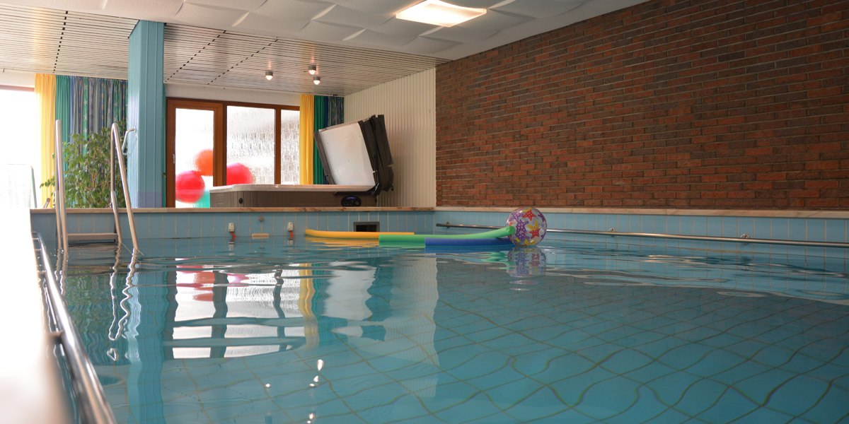 Indoor pool with blue tiles, colorful swimming noodles and a ball. Window with curtains and brick wall in the background., &copy; Hotel Hochwald
