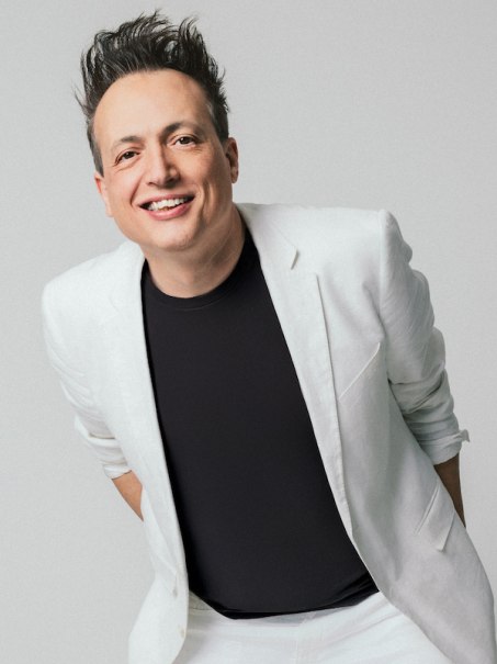 Eine l&auml;chelnde Person in einem wei&szlig;en Anzug und schwarzem T-Shirt vor einem neutralen Hintergrund., &copy; Rosenau Kultur e.V.