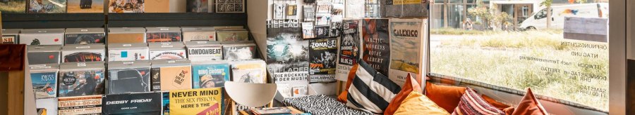 A record store with vinyls, posters and a cozy seating area with cushions. Large window front with a view to the outside., © SMG, Sarah Schmid
