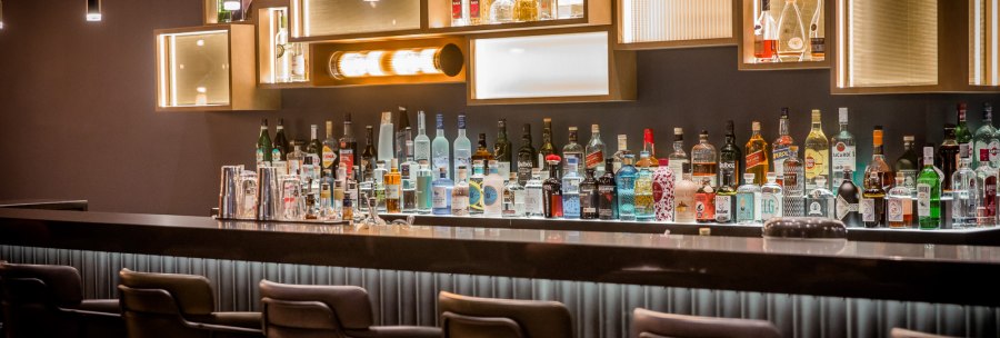 Elegante Bar mit stilvoller Beleuchtung, Flaschen und Gläsern auf der Theke. Moderne Hocker stehen bereit, die Atmosphäre ist gediegen und einladend., © TOMAS Elegante Bar mit stilvoller Beleuchtung, Flaschen und Gläsern auf der Theke. Moderne Hocker stehen bereit, die Atmosphäre ist gediegen und einladend., © TOMAS
