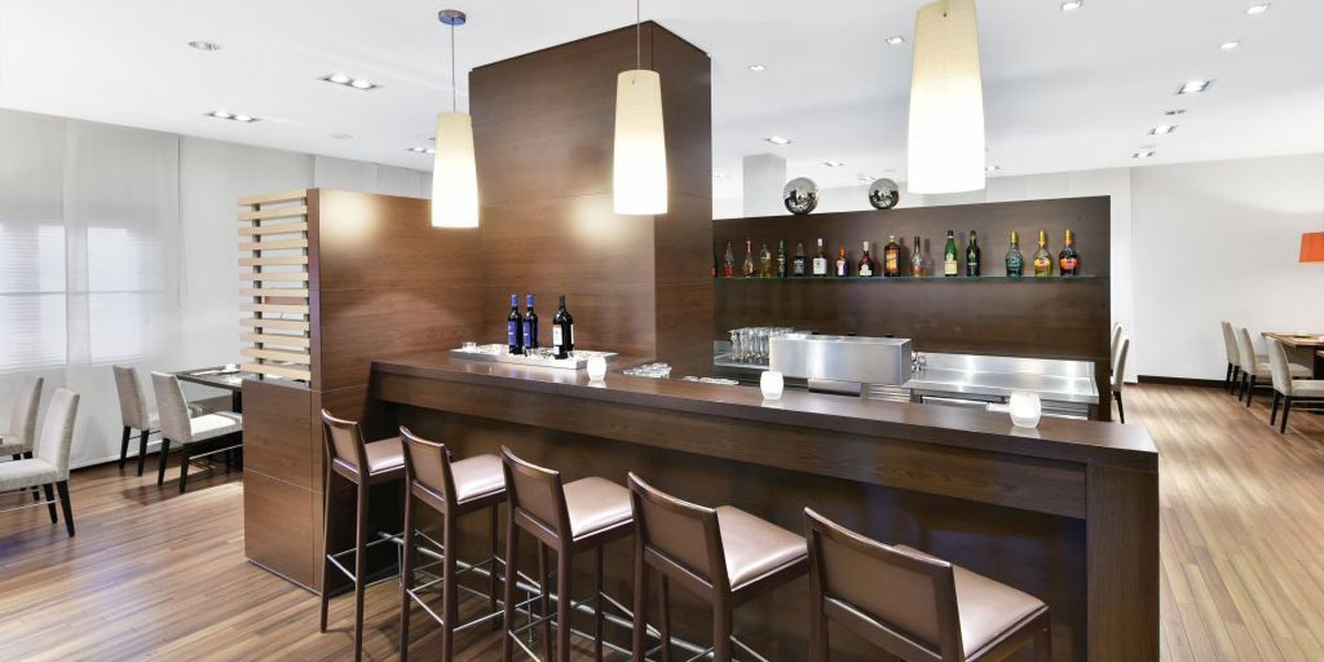 Moderne Bar mit Holztheke, Barhockern und Flaschen im Hintergrund. Helle Beleuchtung und stilvolle Einrichtung., © NH Stuttgart Sindelfingen Moderne Bar mit Holztheke, Barhockern und Flaschen im Hintergrund. Helle Beleuchtung und stilvolle Einrichtung., © NH Stuttgart Sindelfingen