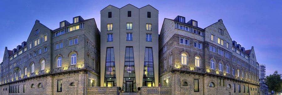 Das Arcotel Camino bei Dämmerung, mit beleuchteten Fenstern und einem klaren Himmel im Hintergrund. Historische Fassade mit modernen Elementen., © www.fnoxx.de