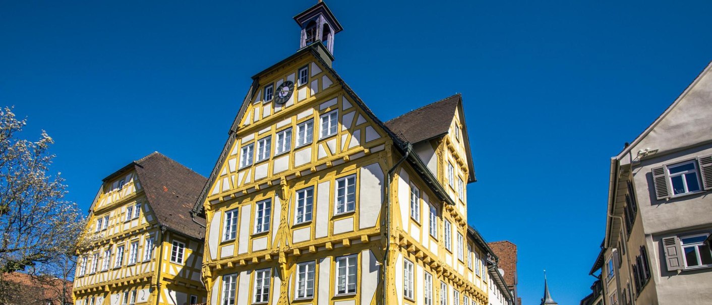 A historic half-timbered house in Sindelfingen, painted yellow and white, under a clear blue sky. A tree in bloom can be seen on the left side of the picture., © SMG Stuttgart Marketing GmbH - Sarah Schmid A historic half-timbered house in Sindelfingen, painted yellow and white, under a clear blue sky. A tree in bloom can be seen on the left side of the picture., © SMG Stuttgart Marketing GmbH - Sarah Schmid