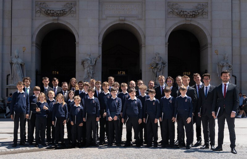 Gruppe von Jungen und Männern in blauen Pullovern vor einem Gebäude mit Bögen und Statuen. Sie posieren für ein Foto., © Knabenchor collegium iuvenum Stuttgart