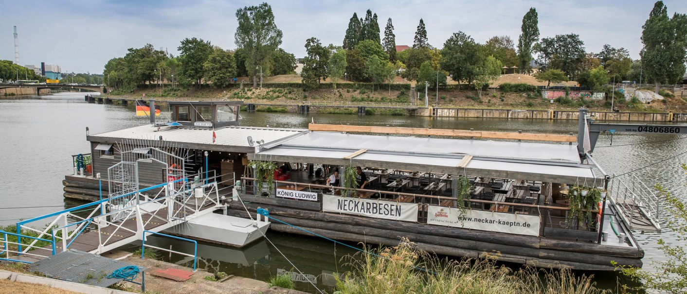 Schwimmendes Restaurant 'Neckarbesen' auf einem Fluss, umgeben von B&auml;umen. Eine Br&uuml;cke ist im Hintergrund sichtbar., &copy; all copyrights are reserved by maks richter