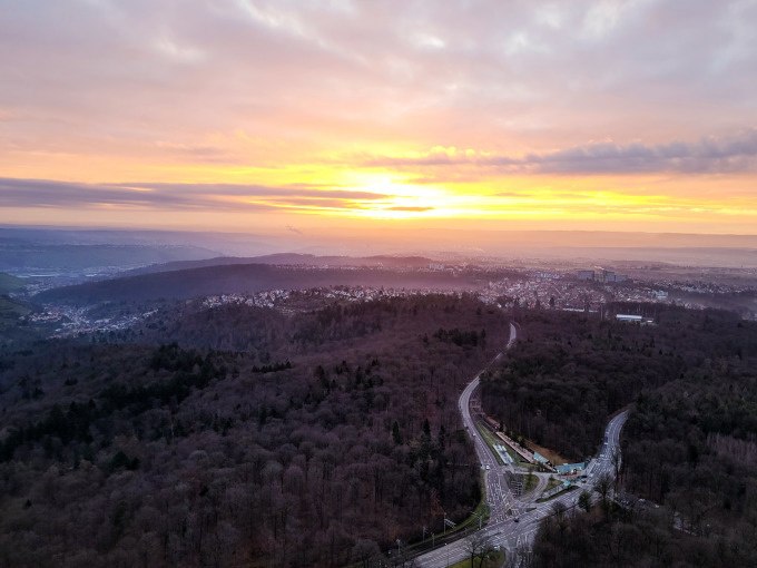 Sunrise over a forested landscape with roads and a city in the background. The sky is partly cloudy, and the sun shines with a yellow-orange glow., © SWR Media Services GmbH / Fernsehturm Stuttgart Sunrise over a forested landscape with roads and a city in the background. The sky is partly cloudy, and the sun shines with a yellow-orange glow., © SWR Media Services GmbH / Fernsehturm Stuttgart