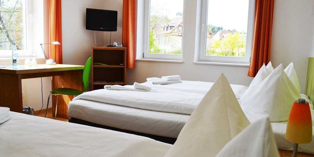 Bright room with two beds, desk, green chair and TV. Large windows with orange curtains., &copy; ECOINN Hotel am Campus