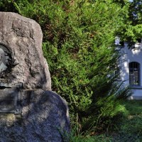 Memorial stone for Gottlieb Daimler in a green park, on the right a white building with glass windows., © Stuttgart-Marketing GmbH Achim Mende