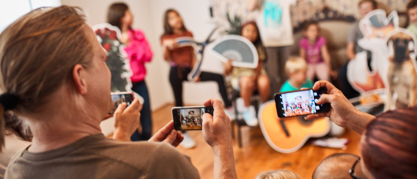 Adults photograph children posing with props. The scene looks lively and playful, with a focus on interaction and fun., © FTGRF.de