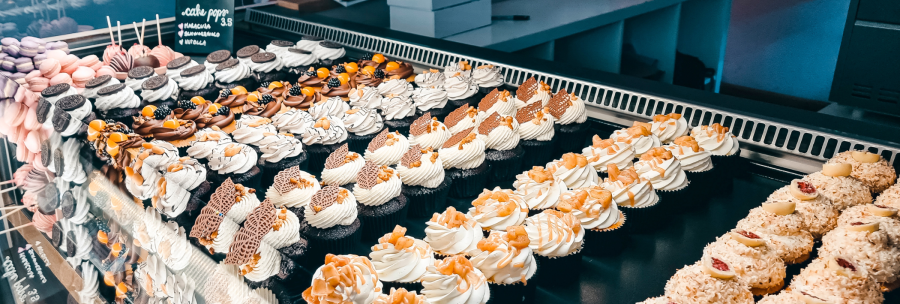 A display case full of colorful cupcakes and macarons, artfully decorated with cream and chocolate., &copy; Cupcakes & Bagels, Stuttgart