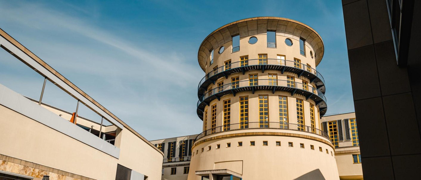 Rundes Gebäude mit modernen Elementen und blauen Balkonen, umgeben von weiteren Gebäudeteilen, unter blauem Himmel., © Stuttgart-Marketing GmbH, Sarah Schmid