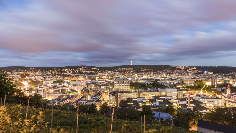 Panorama einer Stadt bei Abenddämmerung, mit beleuchteten Gebäuden und einem bewölkten Himmel im Hintergrund., © SMG, Werner Dieterich