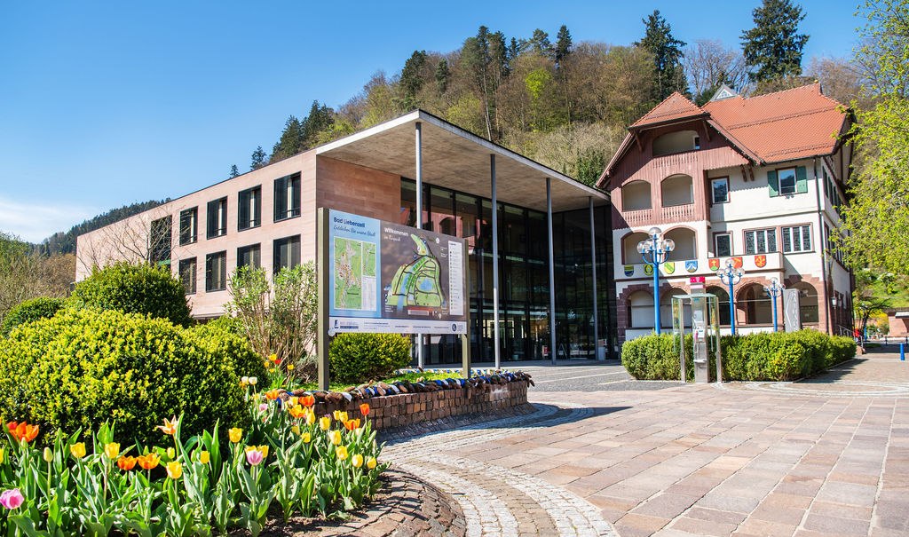 Modern building next to a traditional house in Bad Liebenzell, surrounded by colorful flowers and trees, under a blue sky., © LOCHER Fotodesign&Manufaktur (LOCHER Fotodesign&Manufaktur (Photographer) - [None] (LOCHER Fotodesign&Manufaktur (LOCHER Fotodesign&Manufaktur (Photographer) - [None] (Photographer) - [None]