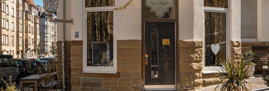 Eingang des Caf&eacute; Seyffer&rsquo;s an einer Stra&szlig;enecke, dekoriert mit goldenen Girlanden und Pflanzen. Die Stra&szlig;e ist von Wohnh&auml;usern ges&auml;umt., &copy; SMG, Sarah Schmid