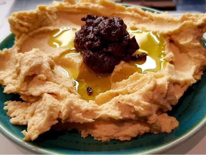 Creamy hummus on a plate, garnished with olive oil and a dark paste in the center., © Kultweine-Kochwelten-Kunstücke - Kochschule Sonja Lenz Creamy hummus on a plate, garnished with olive oil and a dark paste in the center., © Kultweine-Kochwelten-Kunstücke - Kochschule Sonja Lenz
