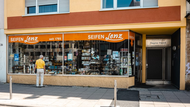 Ein Mann betrachtet das Schaufenster des Geschäfts 'Seifen Lenz', das seit 1785 besteht. Das Gebäude hat eine orangefarbene Markise., © SMG Stuttgart Marketing GmbH - Sarah Schmid Ein Mann betrachtet das Schaufenster des Geschäfts 'Seifen Lenz', das seit 1785 besteht. Das Gebäude hat eine orangefarbene Markise., © SMG Stuttgart Marketing GmbH - Sarah Schmid