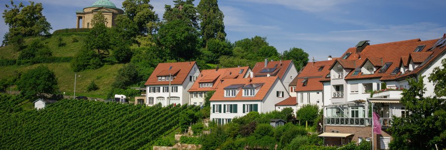 Weinberge mit roten Dachhäusern, im Hintergrund eine Kapelle auf einem bewaldeten Hügel unter blauem Himmel., © Rotenberger Weingärtle, Frederik Garlin Weinberge mit roten Dachhäusern, im Hintergrund eine Kapelle auf einem bewaldeten Hügel unter blauem Himmel., © Rotenberger Weingärtle, Frederik Garlin