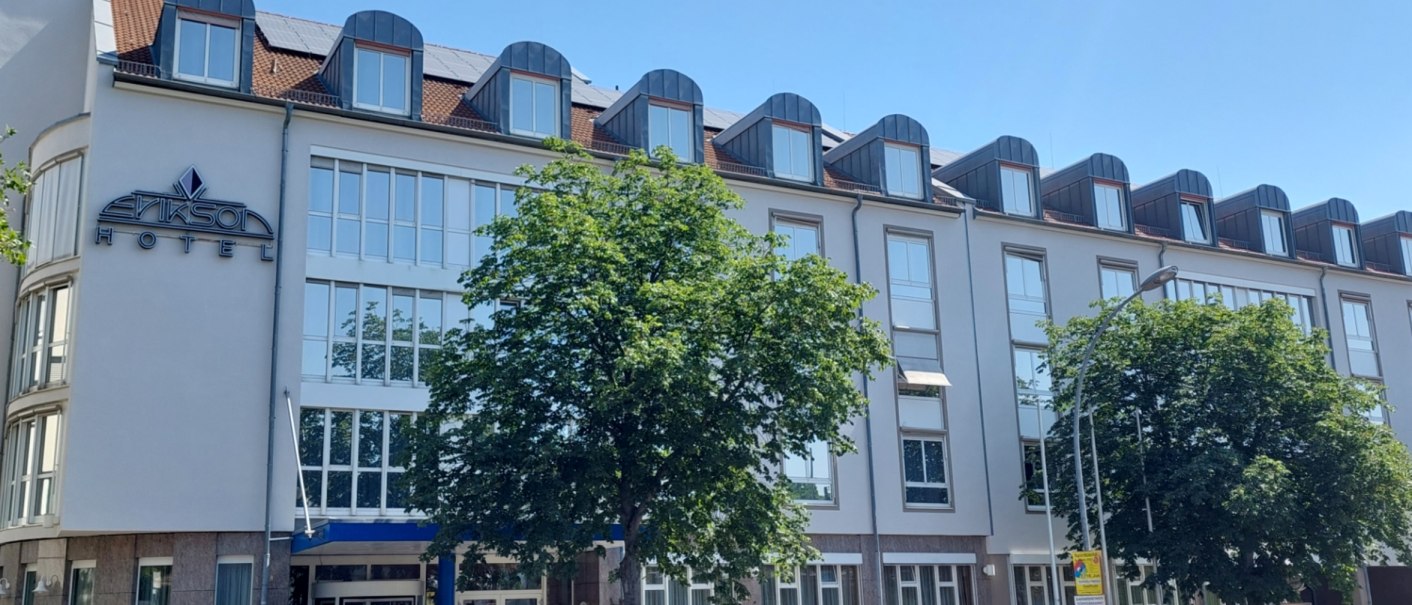 Modern hotel fa&ccedil;ade with large windows and dormer windows, a tree and a car in front of it. Clear, sunny weather conditions., &copy; Erikson Hotel