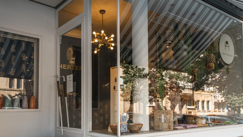 Schaufenster eines Geschäfts namens 'Von Herzen', dekoriert mit Pflanzen, Lampen und Körben. Die Spiegelung zeigt eine Straße mit Gebäuden., © SMG, Sarah Schmid