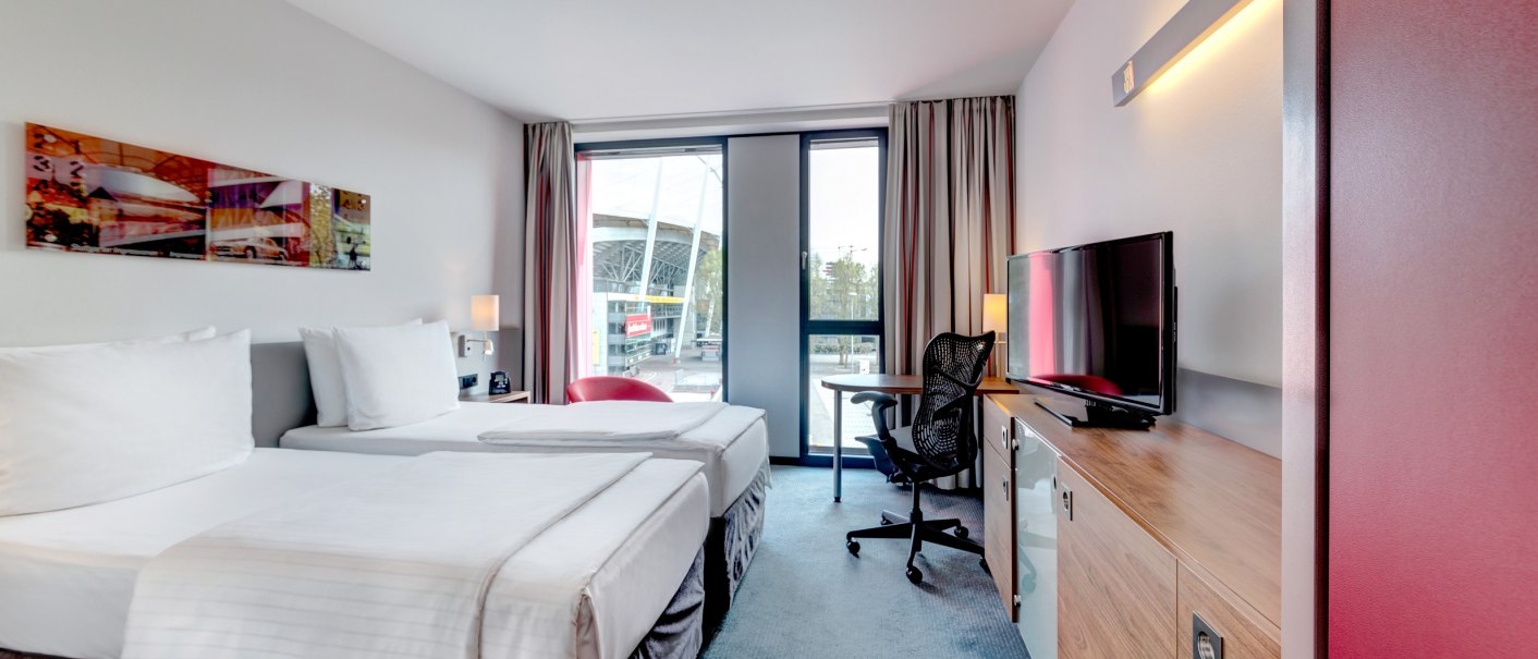 Modernes Hotelzimmer mit zwei Einzelbetten, Schreibtisch, Stuhl und Fernseher. Gro&szlig;e Fenster bieten Blick nach drau&szlig;en. Helle, freundliche Einrichtung., &copy; Hilton Garden Inn Stuttgart Neckarpark