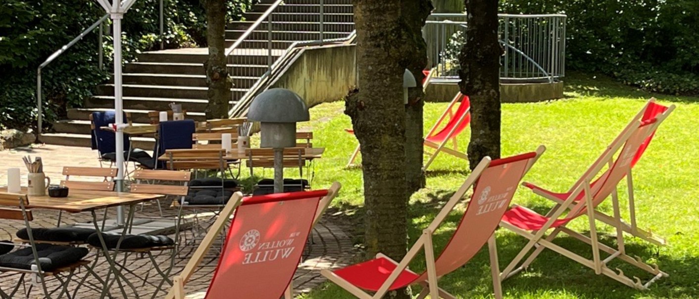 A garden with red sun loungers and wooden tables under white parasols, surrounded by trees and a staircase in the background., © Holiday Inn Stuttgart A garden with red sun loungers and wooden tables under white parasols, surrounded by trees and a staircase in the background., © Holiday Inn Stuttgart