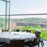 A round table with a white tablecloth and glasses stands in a glassed-in room with a view of a city and historic buildings., © Stuttgart-Marketing GmbH A round table with a white tablecloth and glasses stands in a glassed-in room with a view of a city and historic buildings., © Stuttgart-Marketing GmbH