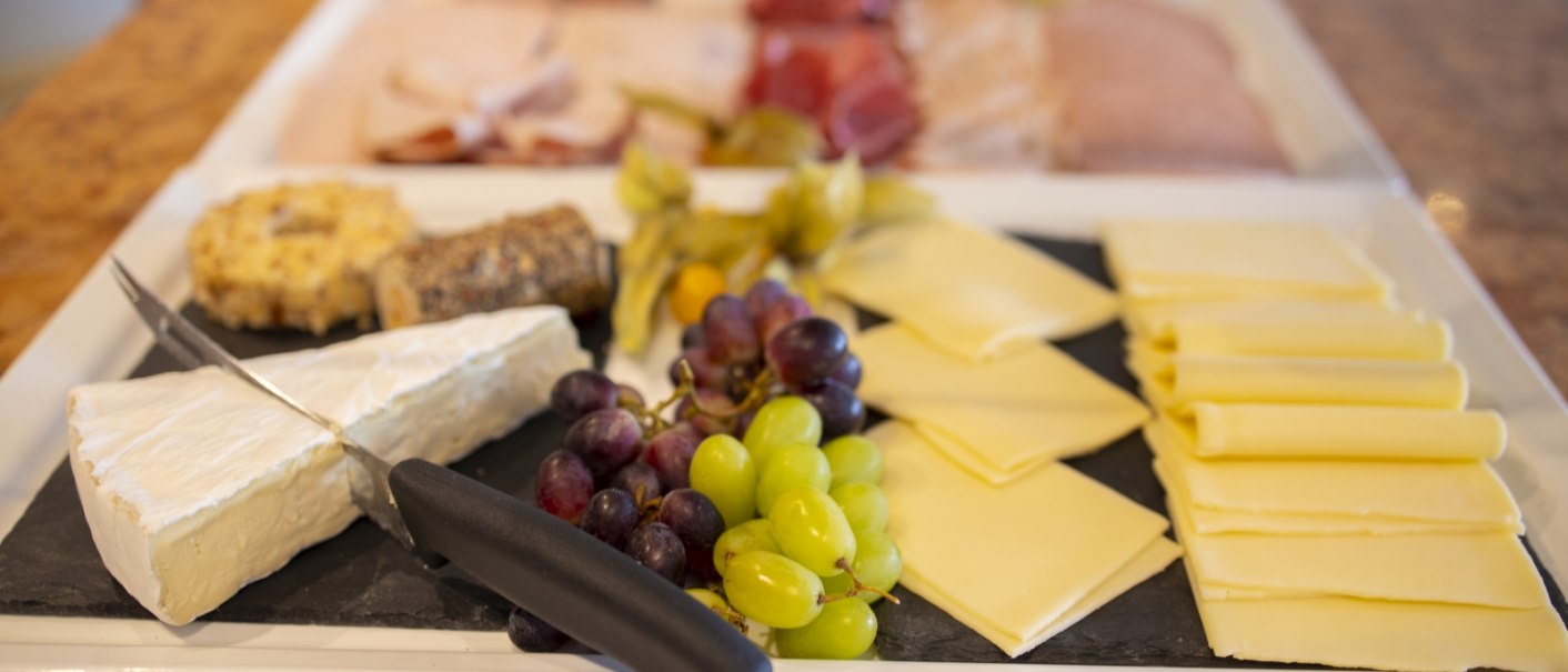 A breakfast buffet with various cheeses, grapes and cold cuts. In the foreground, a knife lies on a piece of Brie., © Hotel Gloria GmbH Restaurant Möhringer Hexle A breakfast buffet with various cheeses, grapes and cold cuts. In the foreground, a knife lies on a piece of Brie., © Hotel Gloria GmbH Restaurant Möhringer Hexle