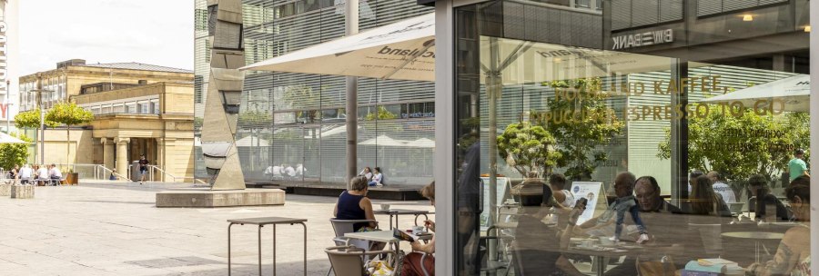 People sitting in a café on a city square. Modern buildings and a work of art can be seen in the background., © SMG Stuttgart Marketing GmbH - Sarah Schmid People sitting in a café on a city square. Modern buildings and a work of art can be seen in the background., © SMG Stuttgart Marketing GmbH - Sarah Schmid