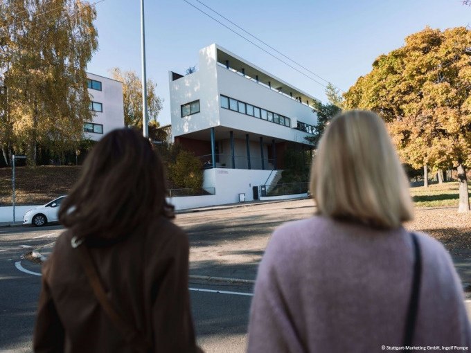 Zwei Personen stehen vor einem modernen Gebäude in der Weissenhofsiedlung, umgeben von herbstlichen Bäumen., © Stuttgart-Marketing GmbH, Ingolf Pompe