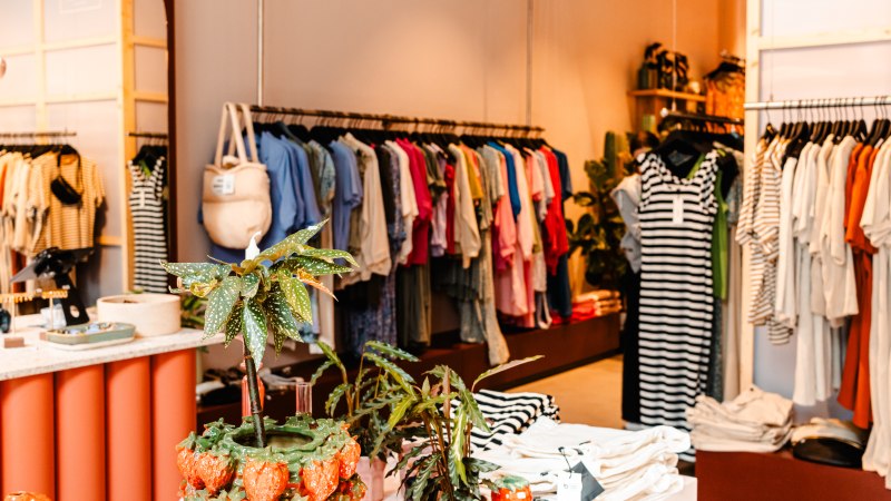 A clothing store with colorful clothes on clothes rails, plants and a mirror in the background., &copy; Sarah Schmid