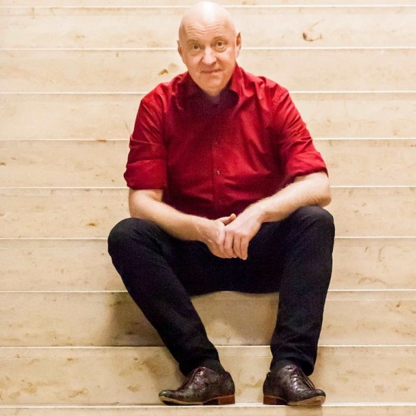 A person in a red shirt sits relaxed on a light-colored marble staircase and looks into the camera., &copy; Renitenztheater Stuttgart e.V.