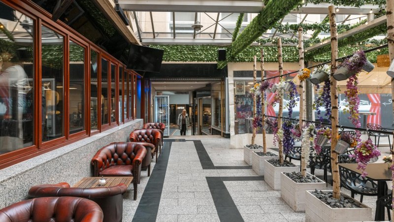 A cozy courtyard with red leather armchairs, decorative plants and a glass roof. A person enters the area in the background., © SMG Stuttgart Marketing GmbH - Sarah Schmid