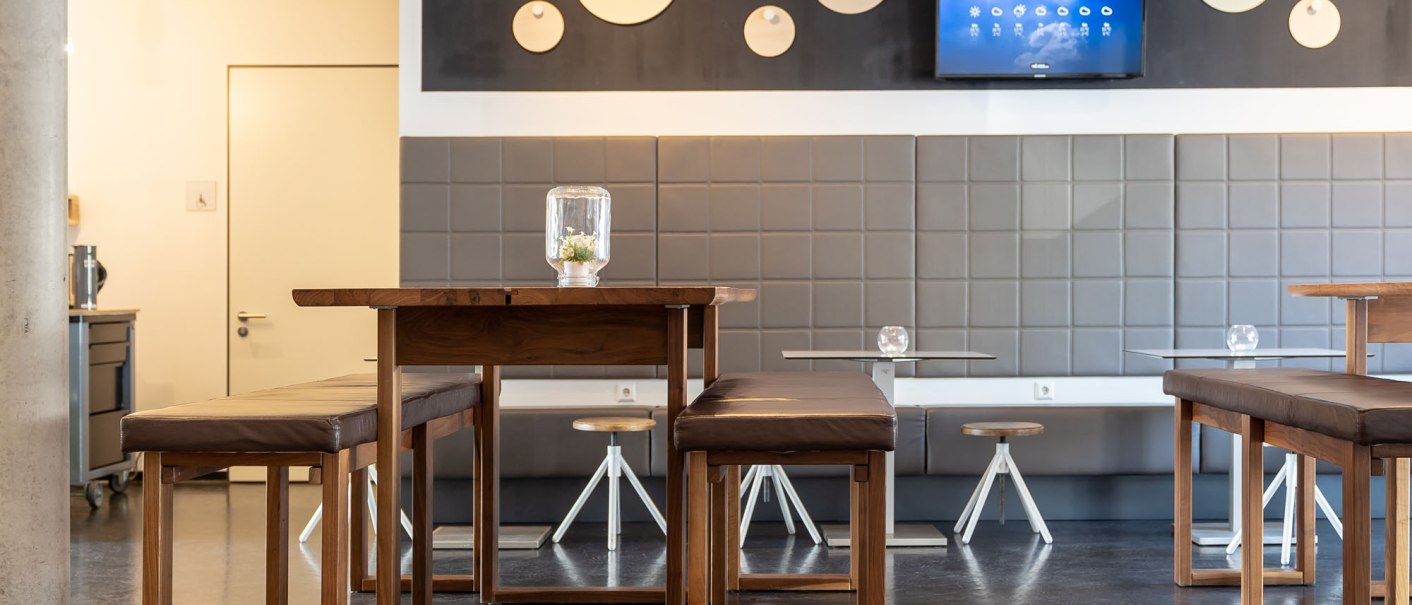 Modern lobby with wooden tables and upholstered benches. Decorative circles and a screen hang on the wall. Subtle lighting., &copy; a2 HOTELS