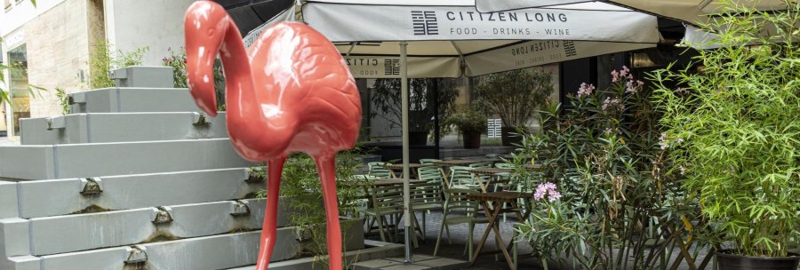 A large, pink flamingo stands in front of the Citizen Long caf&eacute;. Tables, chairs and plants can be seen in the background., &copy; SMG, Sarah Schmid