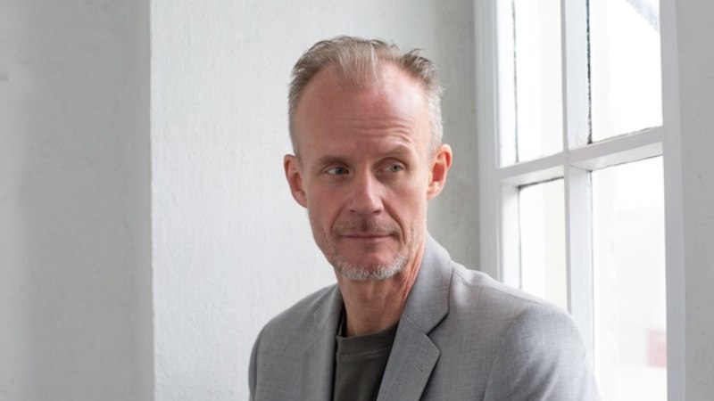 A man leans relaxed against a wall and looks confidently into the camera. He has a light beard and short hair., &copy; Renitenztheater Stuttgart e.V.