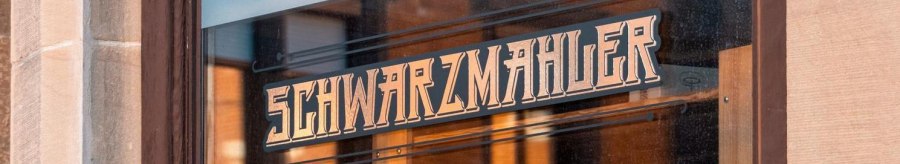 A shop window with the lettering 'Schwarzmahler' in stylized script. The surroundings are reflected in the glass., © SMG Stuttgart Marketing GmbH - Sarah Schmid A shop window with the lettering 'Schwarzmahler' in stylized script. The surroundings are reflected in the glass., © SMG Stuttgart Marketing GmbH - Sarah Schmid