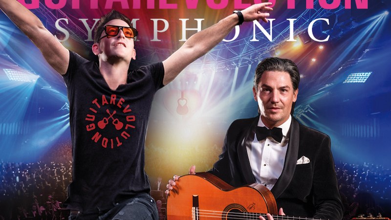 Zwei Männer vor einer Konzertkulisse. Einer trägt eine Gitarre und einen Anzug, der andere ein T-Shirt mit ausgestreckten Armen. Hintergrund zeigt Lichter und Publikum., © Shooter Promotions GmbH Zwei Männer vor einer Konzertkulisse. Einer trägt eine Gitarre und einen Anzug, der andere ein T-Shirt mit ausgestreckten Armen. Hintergrund zeigt Lichter und Publikum., © Shooter Promotions GmbH