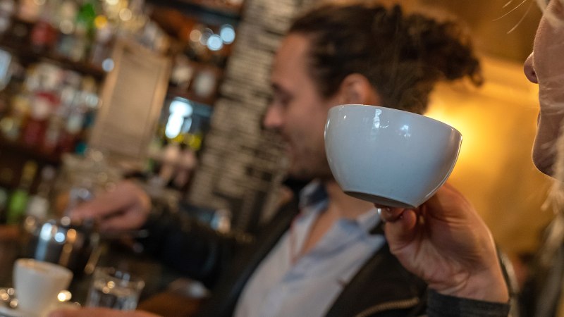 Two people in a caf&eacute;. One person is drinking from a cup while the other prepares coffee. Shelves with bottles can be seen in the background., &copy; Stuttgart Marketing  GmbH, Fotografin Martina Denker, post@denkerfotografie.de