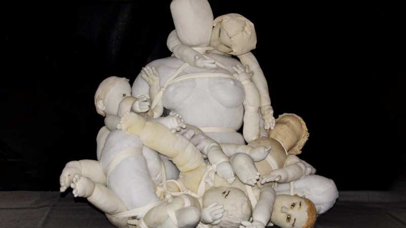 Eine ausdrucksstarke Stoffskulptur zeigt eine Frauengestalt, umgeben von mehreren festgebundenen Kindern. Die Figuren sind in hellen Tönen gehalten., © Min Bark Eine ausdrucksstarke Stoffskulptur zeigt eine Frauengestalt, umgeben von mehreren festgebundenen Kindern. Die Figuren sind in hellen Tönen gehalten., © Min Bark