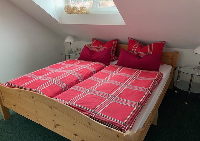 Gemütliches Schlafzimmer mit einem Holzbett, roten karierten Bettbezügen und zwei Nachttischen unter einem Dachfenster., © Weinhof am Württemberg Gemütliches Schlafzimmer mit einem Holzbett, roten karierten Bettbezügen und zwei Nachttischen unter einem Dachfenster., © Weinhof am Württemberg