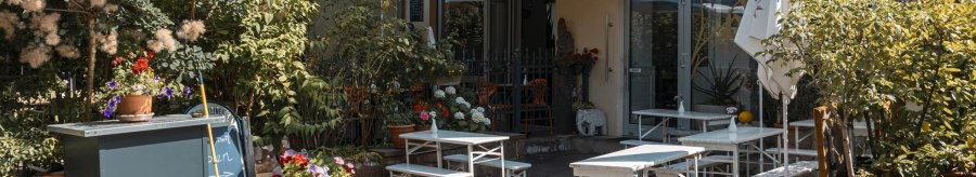 Cosy outdoor area of a café with white tables and chairs, surrounded by lush plants and colorful flowers., © SMG Stuttgart Marketing GmbH - Sarah Schmid