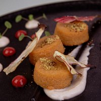 Gourmet dish on a black plate, decorated with sauces, herbs and vegetables. Elegant arrangement with different textures and colors., © Marc Luppa